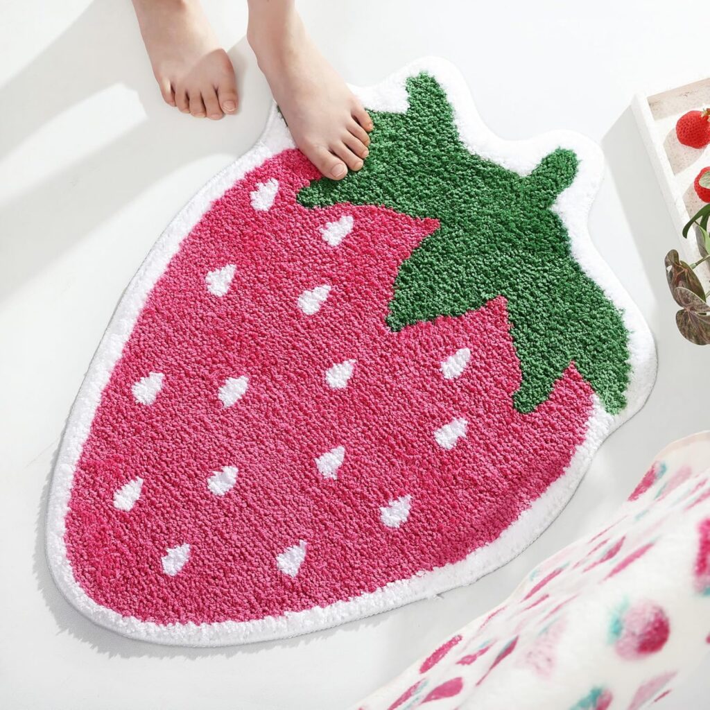 Cute pink strawberry-shaped bath mat made from soft absorbent microfiber with non-slip latex backing, designed as a playful fruit-themed bathroom rug for showers, bathtubs, bedrooms, and whimsical pink room décor.