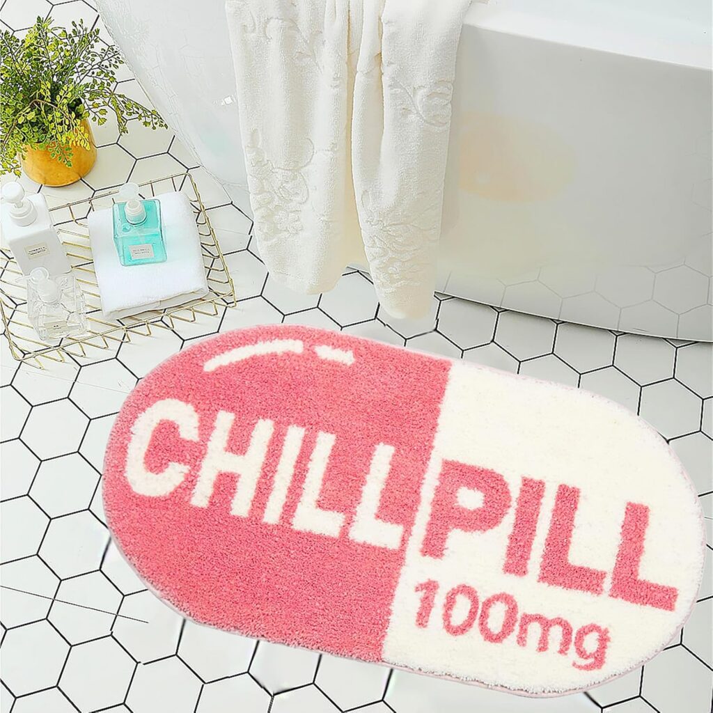 Pink chill pill-shaped bath mat with soft microfiber plush pile, absorbent surface, and non-slip TPR backing, designed as a fun novelty bathroom rug for showers, tubs, bedrooms, and playful pink room décor.