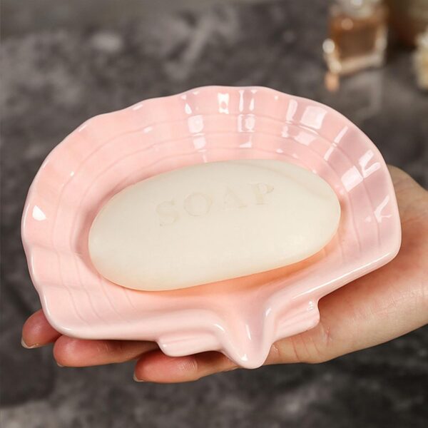 Pink ceramic seashell soap dish with a self-draining sloped design, glazed finish, and anti-slip base for keeping bar soap dry on bathroom sinks, showers, and vanity countertops.